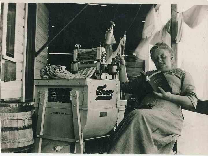 Woman reading next to one of the first washing machines